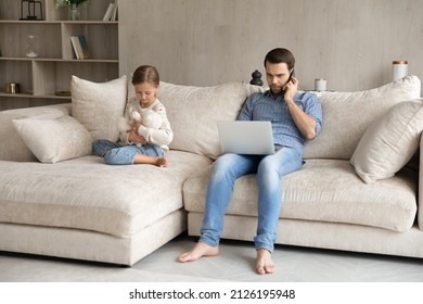 Serious distant employee father working from home, speaking on cellphone, consulting internet, reading email on laptop, sitting on couch, ignoring little daughter girl huggin toy teddy bear - Shutterstock ID 2126195948