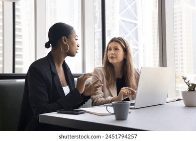 Serious diverse business colleagues meeting in coworking cafe, talking at laptop, discussing work project. Young businesswoman consulting African advisor, legal expert, agent - Powered by Shutterstock