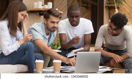 Serious Diverse Friends Study Together With Laptop And Notebooks Prepare For Exam In Cafe, Focused Multiracial Young People Group Talking Using Computer Sitting On Coffee House Terrace Doing Research