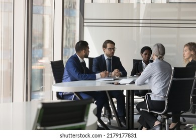 Serious Diverse Group Of Business Coworkers Collaborating On Project. Business Partners Negotiating On Deal, Discussing Agreement Terms At Meeting Table In Modern Office Space Interior