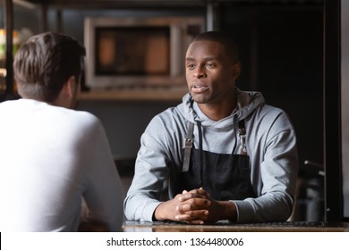 Serious diverse males talking inside cafe, african chef interviewing the candidate for position at restaurant kitchen, restaurateur business owner negotiating with grocery supplier or partner concept - Powered by Shutterstock