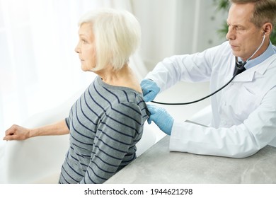 Serious Doctor Examining Old Woman With Stethoscope In Clinic