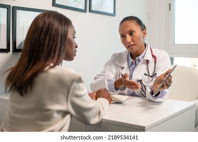 Serious Doctor Explaining Diagnosis Showing Touchpad To Patient. Young African American Woman Sitting In Doctors Office And Listening To General Practitioner. Medical Consultation Concept