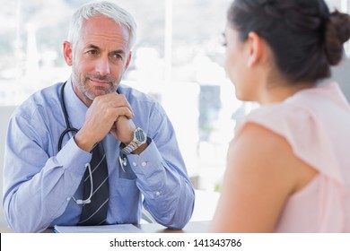 Serious Doctor Listening To Patient Explaining Her Painful In His Office