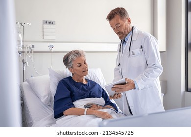 Serious doctor showing on digital tablet the medical report and health results to senior patient. Old woman sitting on hospital bed listening surgeon while explaining surgery procedure. Consultation - Powered by Shutterstock