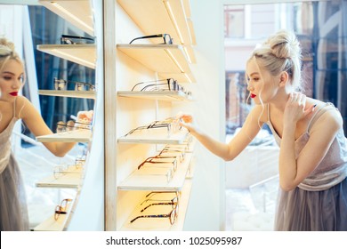 Serious elegant fasionable woman with red lips choosing eyeglasses in optical store - Beautiful girl wearing eyeglasses in optician shop. Ophthalmology concept. - Powered by Shutterstock