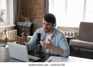 Serious Engaged Business Professional Man Speaking At Online Conference, Using Microphone, Wireless Headphones, Laptop Computer At Home Office Work Table, Making Video Call, Talking, Explaining