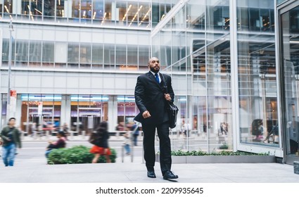 Serious Executive Bald Bearded Black Man In Suit Carrying Stylish Leather Bag While Walking In Business Center On Background Of Glass Windows And People Crowd