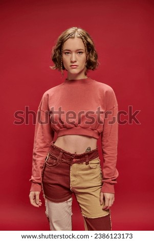 serious face, tattooed fashion model posing in patchwork pants and cropped long sleeve on red