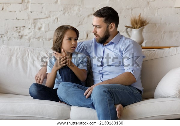 Serious father listen to his pre-teen little son\
talking seated on sofa at home, speaking spend time together at\
home. Cute boy share problems, ask advice to dad. Communication,\
care and trust concept