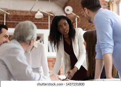 Serious female black executive discussing disputing on work issues with male caucasian colleague at corporate office briefing, business team talk solve problem brainstorm in teamwork at group meeting