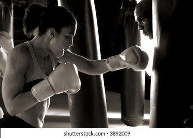Serious female boxer throwing a right cross at the heavy bag being held by her trainer while he looks around the bag