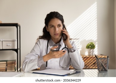 Serious Female Doctor Giving Telephone Consultation, Talking To Patient On Cellphone, Making Phone Call From Clinic Office. General Practitioner Working On Healthcare Hotline, Answering Questions