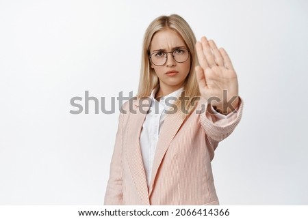Serious female entrepreneur stretching out hand in stop sign, prohibit, forbid something, saying no, standing over white background in suit and glasses