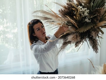 Serious Female Host Making Big Bouquet Of Dried Flowers And Plants For Christmas Celebration Party At Home