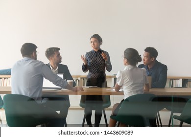 Serious female indian manager talk at diverse group meeting consult clients in boardroom behind glass door, multicultural business people with woman team leader discuss work at corporate briefing