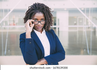 Serious Female Office Employee Touching Eyewear Outside. Young African American Business Woman Standing At Glass Wall, Adjusting Glasses, Looking At Camera. Vision Concept