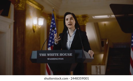 Serious female politician or government representative speaks at press conference for media and television. US minister gives inspirational speech in the White House. American flags in the background. - Powered by Shutterstock