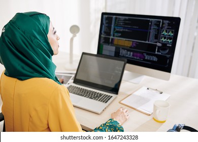 Serious female software engineer working on computer and laptop in her office