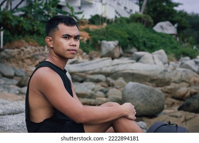 Serious Filipino Man Sitting On Rocks. Pensive Male Person Alone With Contemplating Look Outdoors. Inner Peace Concept