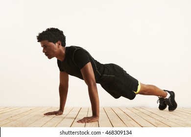 Serious Fit Black African American Man Performing A Pushup From Light Wooden Floor Against A White Wall