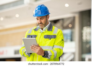 Serious and focused architect or engineer working on construction site using digital tablet. Mature man working on digital tablet at construction site. Mid adult manual worker checking list on laptop. - Powered by Shutterstock