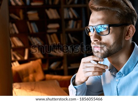 Serious focused businessman wearing computer glasses looking at pc screen with computer reflection using internet, watching webinar training, working online by video conference, close up face view.