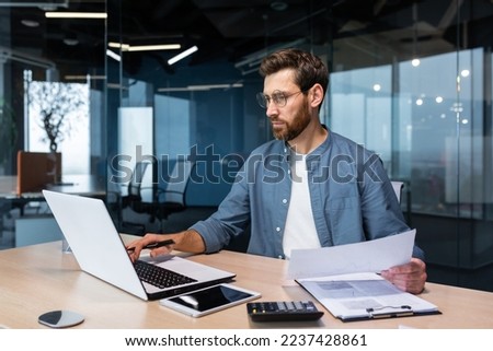 Serious and focused financier accountant on paper work inside office, mature man using calculator and laptop for calculating reports and summarizing accounts, businessman at work in casual clothes. Foto d'archivio © 