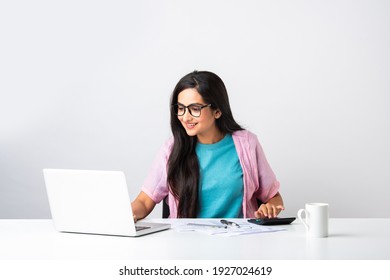 Serious Focused Indian Businesswoman Or House Wife Holding Papers Preparing Report ,analyzing Work Results, Doing Paperwork At Workplace Using Computer Online Software