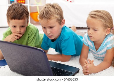 Serious And Focused Kids Looking At Laptop Computer Laying On The Floor