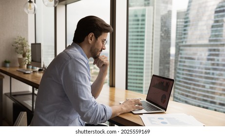 Serious focused man in glasses sit at workplace table looks at laptop monitor work with financial project statistics, analyzing incomes seen in charts and graphs. Business analysis, strategy concept