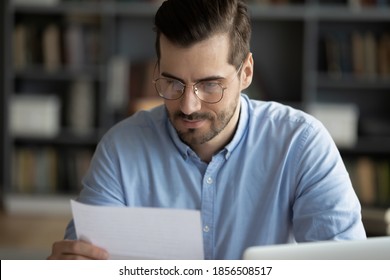 Serious focused man sitting at workplace desk holding paper sheet reading news in correspondence learn written information in formal business letter, legal notification from bank, got proposal concept