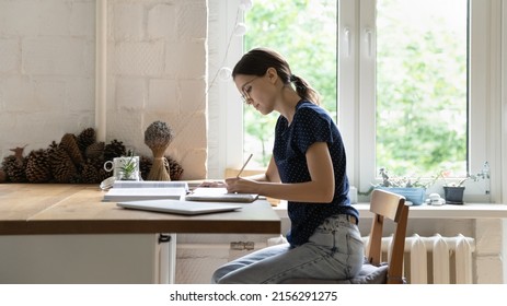 Serious Focused Smart Hardworking Student Wearing Glasses, Preparing For Exam At Home. Young College Girl Writing Essay In Copybook, Studying Book, Making Notes, Summary, Doing School Homework