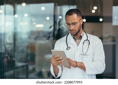 Serious and focused thinking african american doctor using tablet computer, man working inside modern clinic office. - Powered by Shutterstock