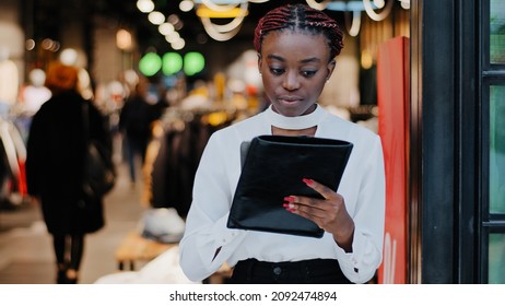 Serious Focused Young African American Girl Salesman Female Worker Busy Woman Clothing Store Owner Stands Indoors Using Digital Tablet Wireless Gadget Device For Inventory Products Online Website