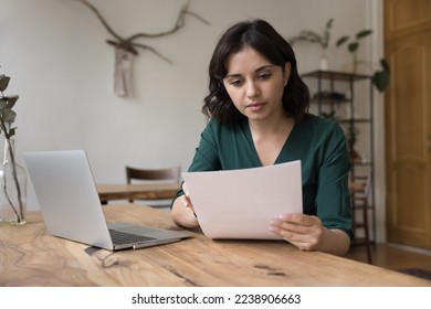 Serious freelance business woman working on report at home, reading document at home office table with laptop, checking bill, invoice, agreement text, sales result, receiving official letter - Powered by Shutterstock