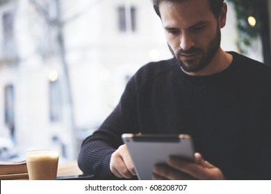 Serious Freelancer Dressed In Casual Outfit Focus On Reading News And Looking On Digital Tablet While Sitting In Cozy Urban Cafe. Young Man Using Modern Technology For Search Job Vacancy In Internet