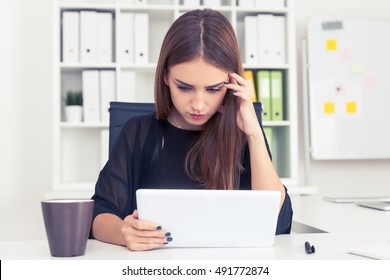 Serious girl in black is looking at her tablet computer screen. Concept of perfectionism at work and everyday life