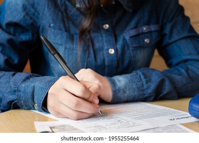 Serious girl model signs the release, there is a red mug on the table, blue glasses case and a smartphone, a woman in a denim shirt. close-up - Shutterstock ID 1955255464