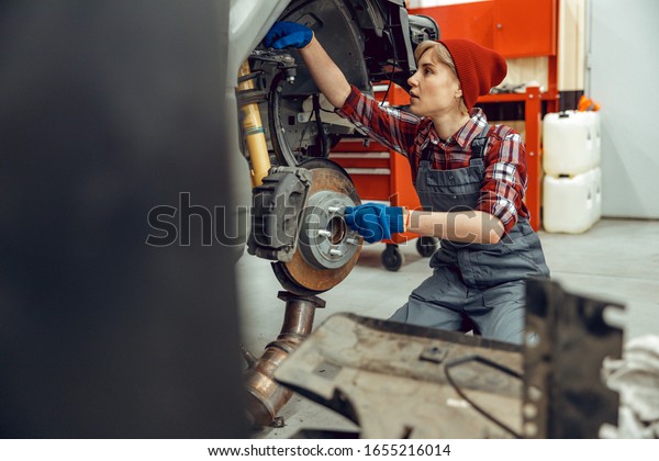 Serious\
girl in work clothes working in a car repair\
shop