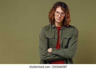 Serious Gloomy Discontent Frowning Irritated Long Curly Hair Young Brunet Man 20s Wears Khaki Shirt Jacket Glasses Hold Hands Crossed Looking Isolated On Plain Olive Green Background Studio Portrait