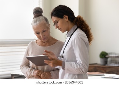 Serious GP doctor showing tablet screen to old 70s female patient, explaining electronic prescription, medical screening, examination result, giving consultation. Woman visiting practitioner - Shutterstock ID 2036344301