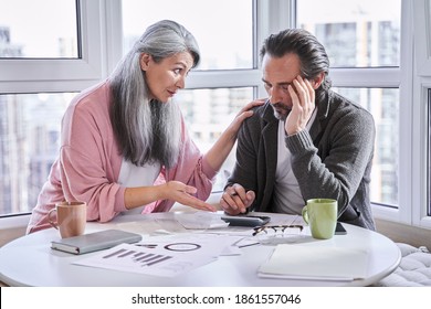 Serious Grey Haired Mature Couple Calculating Bills, Checking Finances Together At Home. Calm Mature Woman Soothes Her Dissapointed Husband