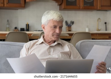 Serious Grey-haired Single Aged Man Sit On Couch With Laptop Holding Bills, Consider Legal Papers, Learn Formal Documents, Pay Utilities On-line, Manage Finances, Do Paperwork, Planning Budget At Home