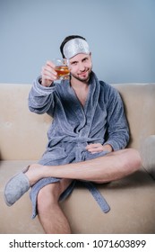 A Serious Guy With A Beard Holds A Glass Of Cola Or Whiskey With Ice In His Hand.Young Playboy In Dressing Gown Toasting With Cocktail.Happy Young Man In Dressing Gown Drinking Martini