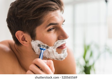 Serious guy shaving his beard