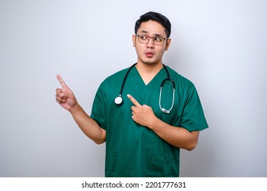 Serious Handsome Asian Doctor, Nurse In Scrubs And Stethoscope, Pointing Fingers Upper Left Corner, Showing Online Clinic Banner, White Background