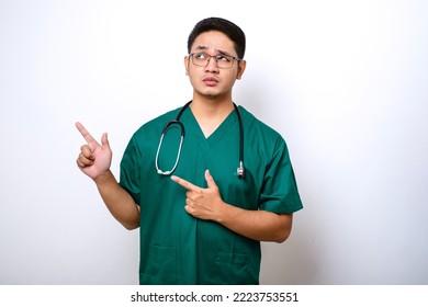 Serious Handsome Asian Doctor, Nurse In Scrubs And Stethoscope, Pointing Fingers Upper Left Corner, Showing Online Clinic Banner, White Background