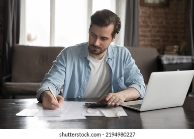 Serious handsome computer user man doing accounting job, checking paper bills, receipts, writing notes in documents, using calculator, counting budget, tax, rent, mortgage fees. Finance management - Powered by Shutterstock