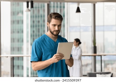 Serious handsome doctor man using medical online application on tablet for job, typing, reading clinic records, electronic database, working with digital device, chatting with patient - Powered by Shutterstock